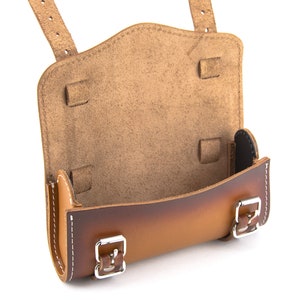 May include: A brown leather saddle bag with two buckles and a flap. The bag is open and the inside is lined with brown suede.