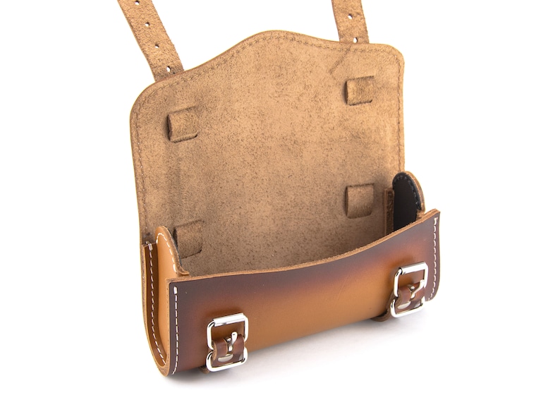 May include: A brown leather saddle bag with two buckles and a flap. The bag is open and the inside is lined with brown suede.