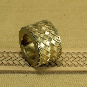 May include: A brass leather stamping tool with a woven pattern. The tool is designed to create a raised, textured design on leather.