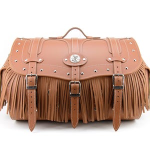 May include: A tan leather saddlebag with fringe, silver studs, and buckles. The bag has a handle and is designed with a flap closure. The bag is a light brown color and has white stitching.