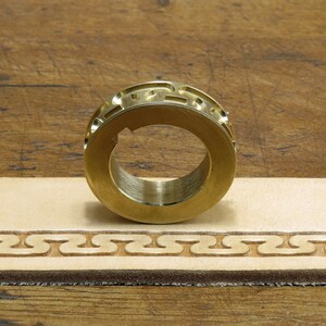 May include: A brass leather stamping tool with a decorative pattern. The tool is used to create a repeating design on leather.