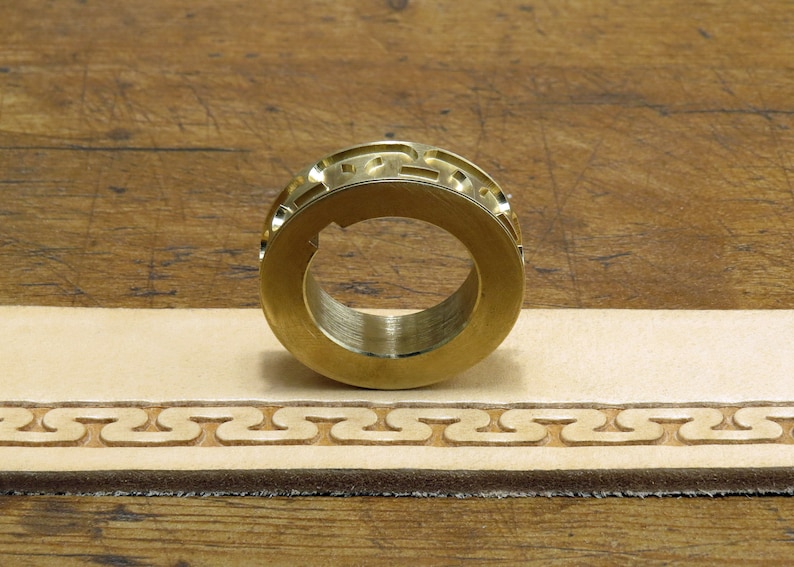 May include: A brass leather stamping tool with a decorative pattern. The tool is used to create a repeating design on leather.