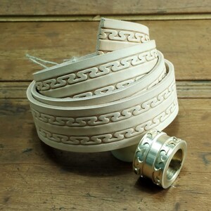May include: A white leather belt with a decorative embossed pattern. The belt is rolled up and a silver metal buckle is shown separately.