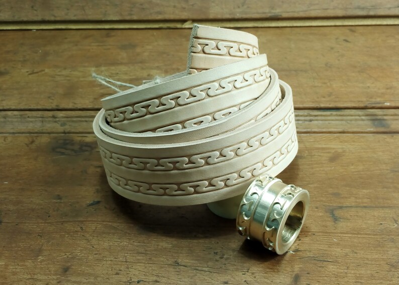 May include: A white leather belt with a decorative embossed pattern. The belt is rolled up and a silver metal buckle is shown separately.