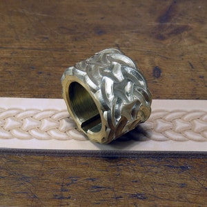 May include: A brass leather stamping tool with a wavy pattern. The tool is lying on a piece of leather that has been stamped with the same pattern.