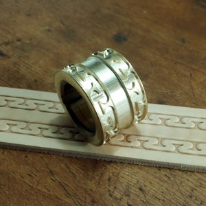 Könnte beinhalten: Ein Lederprägewerkzeug aus Messing mit einem dekorativen Muster. Das Werkzeug ist so konzipiert, dass es ein sich wiederholendes Muster auf Leder erzeugt.