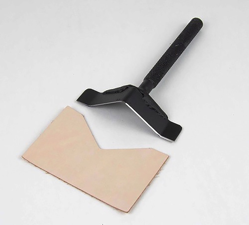 May include: A black leather working tool with a handle and a V-shaped blade. The tool is used to cut leather.