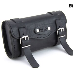 May include: Black leather motorcycle saddlebag with two buckles and a metal plate with the text "ORS" embossed on it.