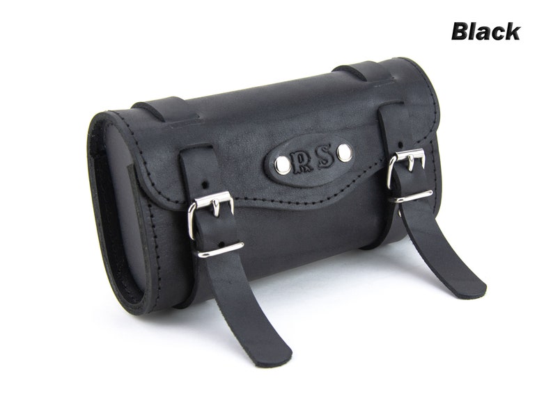 May include: Black leather motorcycle saddlebag with two buckles and a metal plate with the text "ORS" embossed on it.