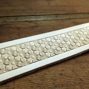 Peut inclure: Gros plan d'une bande de cuir blanc avec un motif en relief r&eacute;p&eacute;t&eacute; de petites fleurs stylis&eacute;es.