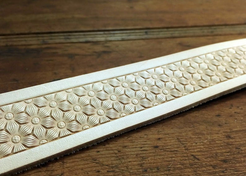 Peut inclure: Gros plan d'une bande de cuir blanc avec un motif en relief r&eacute;p&eacute;t&eacute; de petites fleurs stylis&eacute;es.
