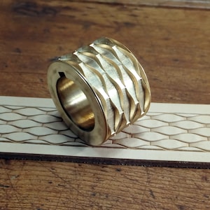 May include: A brass leather stamping tool with a wavy pattern. The tool is lying on a piece of leather that has been stamped with the same pattern.