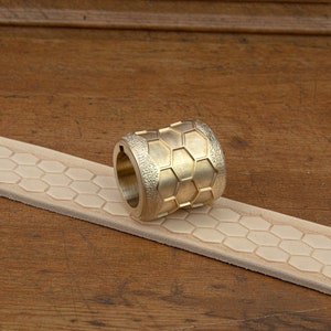 May include: A brass roller tool with a hexagonal pattern, used for creating embossed designs on leather.