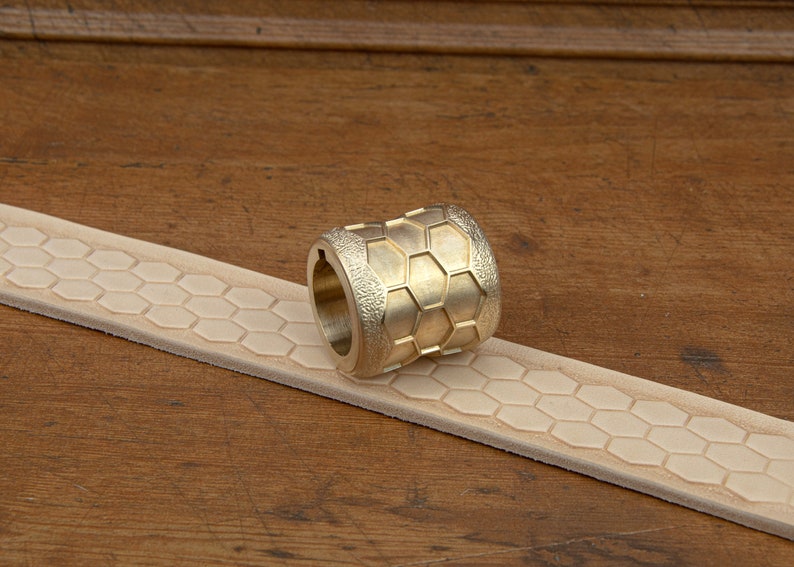 May include: A brass roller tool with a hexagonal pattern, used for creating embossed designs on leather.