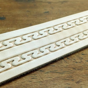 May include: A close-up of a light brown leather strap with two rows of embossed, repeating, wavy patterns.