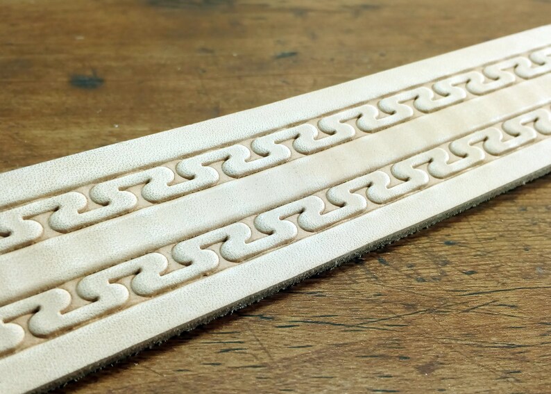 May include: A close-up of a light brown leather strap with two rows of embossed, repeating, wavy patterns.
