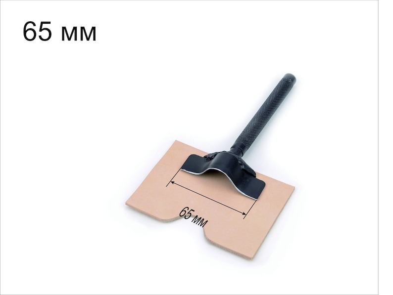 May include: A black leather punch tool with a 65 mm diameter, shown on a piece of brown leather. The tool has a black handle and a metal base.