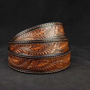 May include: Three brown leather belts with a floral design, stacked on top of each other. The belts have a black background and a brown floral pattern.