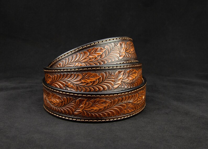 May include: Three brown leather belts with a floral design, stacked on top of each other. The belts have a black background and a brown floral pattern.