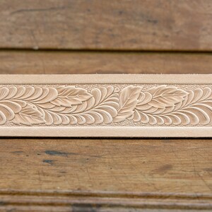 May include: A close-up of a light brown leather strip with a detailed floral design embossed into the surface.