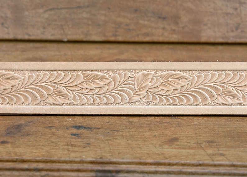 May include: A close-up of a light brown leather strip with a detailed floral design embossed into the surface.