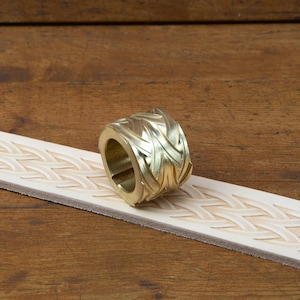 May include: A brass leather stamping tool with a geometric pattern. The tool is lying on a piece of leather that has been stamped with the same pattern.