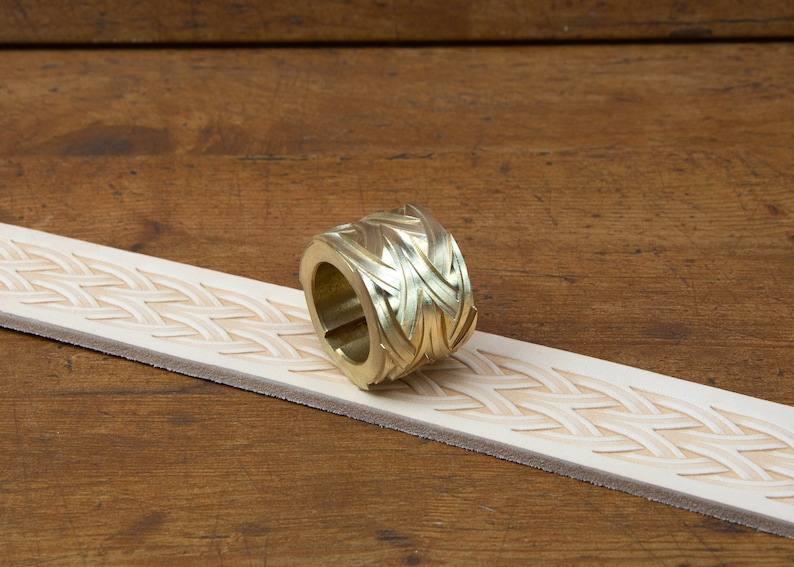 May include: A brass leather stamping tool with a geometric pattern. The tool is lying on a piece of leather that has been stamped with the same pattern.