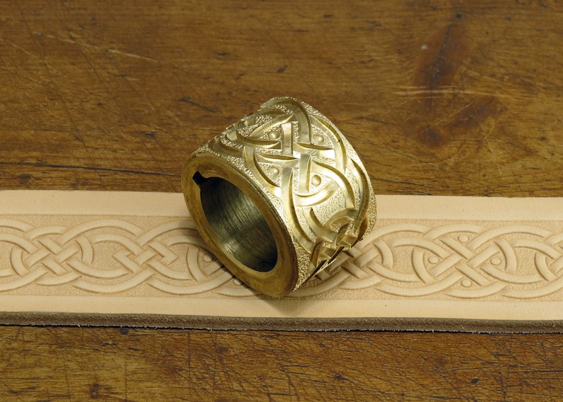 May include: A brass leather stamping tool with a Celtic knot design. The tool is used to create decorative patterns on leather.