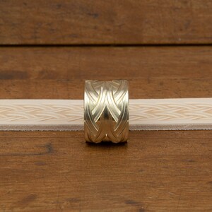 May include: A brass leather stamping tool with a geometric design. The tool is used to create a repeating pattern on leather.