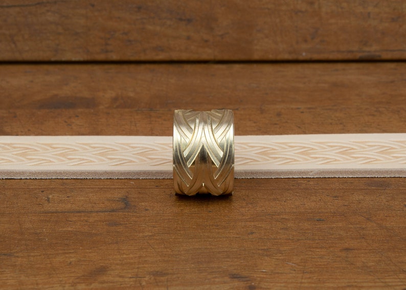 May include: A brass leather stamping tool with a geometric design. The tool is used to create a repeating pattern on leather.