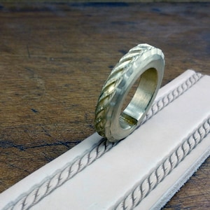 May include: A brass leather stamping tool with a rope design. The tool is being used to create a rope design on a piece of leather.