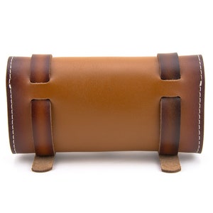 May include: A brown leather roll-up case with white stitching and brown leather straps. The case is closed and has a rounded shape.