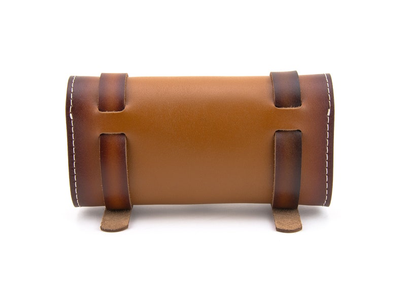 May include: A brown leather roll-up case with white stitching and brown leather straps. The case is closed and has a rounded shape.