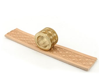 May include: A gold-colored leather stamping tool with a geometric pattern is rolling across a piece of light brown leather. The tool is creating a repeating pattern on the leather.