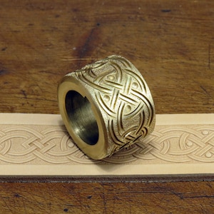 May include: A brass leather stamping tool with a Celtic knot design. The tool is shown on a piece of leather that has been stamped with the same design.