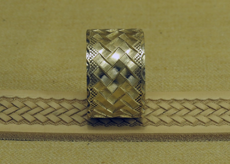 May include: A metal stamp with a geometric pattern of squares and diamonds. The stamp is used to create a decorative design on leather.