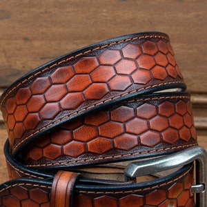 May include: A brown leather belt with a honeycomb pattern and a silver buckle. The belt is folded in half and the buckle is visible.