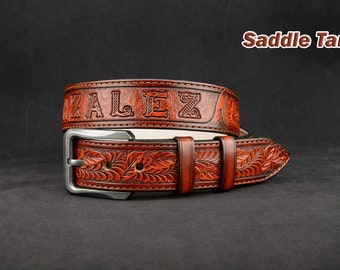 May include: A brown leather belt with a silver buckle. The belt is embossed with a floral pattern and the name "ZALEZ". The belt is labeled "Saddle Tan".