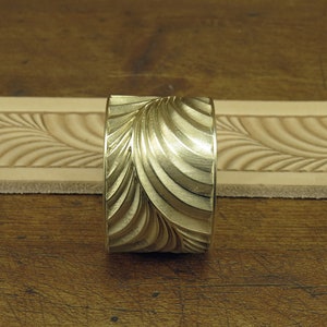 Pu&ograve; includere: Un timbro in metallo dorato con un motivo a spirale ondulato. Il timbro viene utilizzato per creare impressioni decorative sulla pelle.