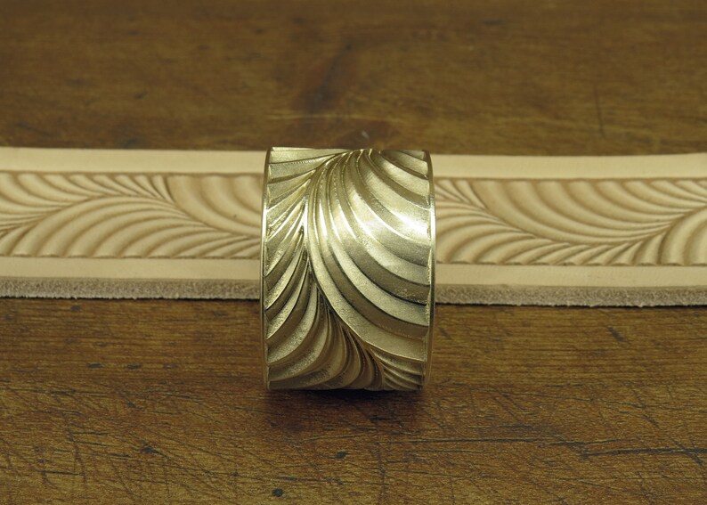 Pu&ograve; includere: Un timbro in metallo dorato con un motivo a spirale ondulato. Il timbro viene utilizzato per creare impressioni decorative sulla pelle.