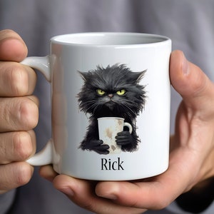 May include: White ceramic mug with a black cat illustration holding a coffee mug. The cat has a grumpy expression and the mug says "Rick" on the bottom.