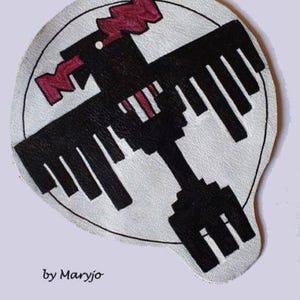 Może przedstawiać: Okrągła, kremowa naszywka z czarno-bordowym geometrycznym wzorem ptaka. Ptak ma stylizowane skrzydło i ogon, z literami "MM" w kolorze bordowym. Tekst "by Maryjo" znajduje się na dole.