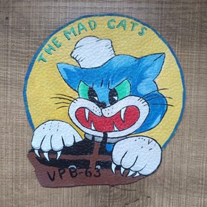 May include: A vintage patch depicting a cartoon blue cat wearing a sailor hat, with green eyes and red fangs. The cat is within a yellow circle, with the words "THE MAD CATS". Below the cat is the text "VPB-63".