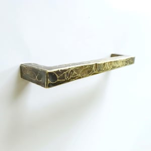 May include: A bronze-colored, rectangular cabinet pull with a textured surface. The hardware is mounted on a white surface. The pull has a hammered appearance, with a dark brown and gold finish.
