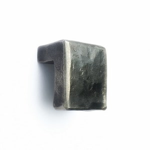 May include: A hammered metal cabinet pull with a rectangular shape and a slightly curved edge. The pull is made of a dark gray metal and has a rustic finish.