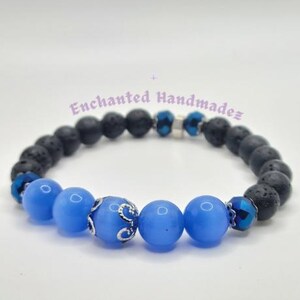 Peut inclure: Un bracelet en perles bleues et noires avec un charme argenté. Le bracelet est composé de perles d'agate bleues et de perles de lave noire.