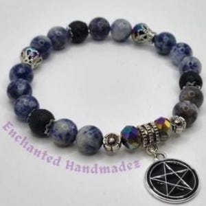 Può includere: Un braccialetto di perline con perline di pietra blu e grigia, perline nere e dettagli argentati. Un ciondolo con un pentagramma nero pende dal braccialetto. Il testo "Enchanted Handmadez" è visibile.