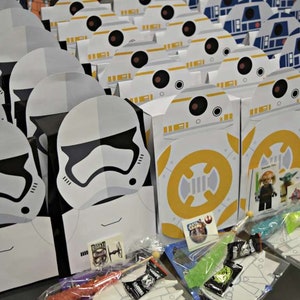 Puede incluir: Una colecci&oacute;n de cajas de regalo para fiestas con tem&aacute;tica de Star Wars con personajes como Stormtroopers y BB-8. Las cajas est&aacute;n llenas de peque&ntilde;os juguetes y golosinas.