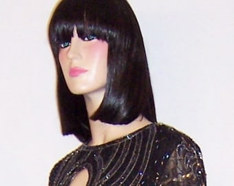 May include: A black sequined dress with silver embroidery and a keyhole neckline. The dress has long sleeves and a fitted silhouette.