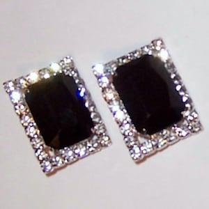 Puede incluir: Un par de pendientes rectangulares negros con un borde de pedrería plateada.